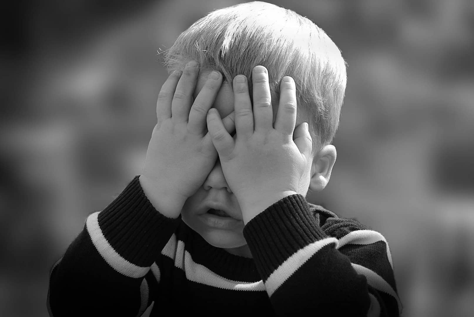 boy in black and white sweater covering his face with his tow hand