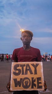 man wearing a hat holding a placard with a text stay woke
