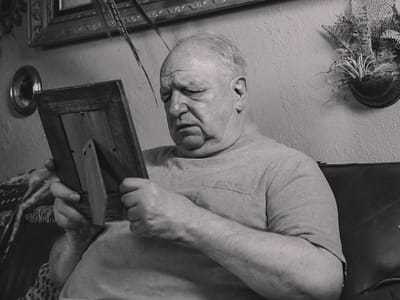 a grayscale photo of an elderly man holding a wooden frame