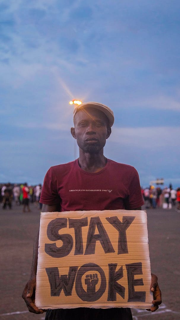 man wearing a hat holding a placard with a text stay woke